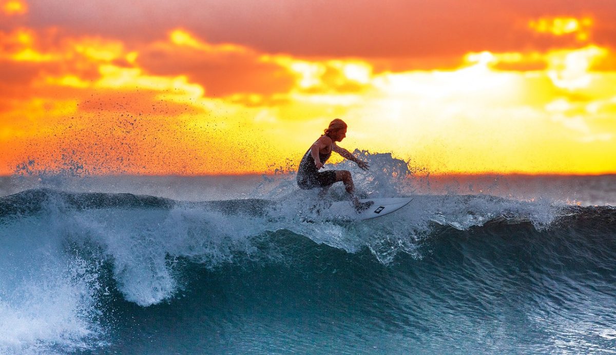 person sufting on large wave with sunset in background