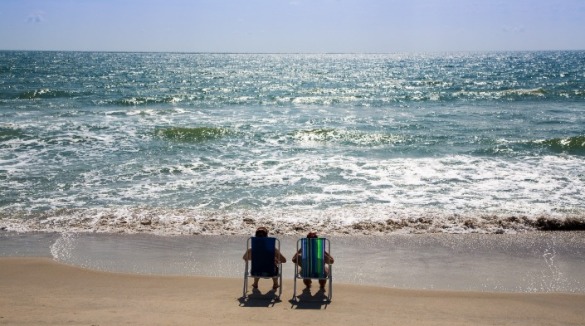 two people sitting on beach looking at ocean